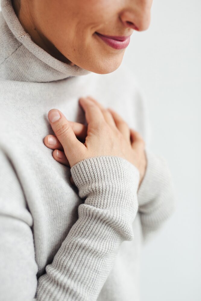 Close-up of a woman in a grey turtleneck with her hand at her chest