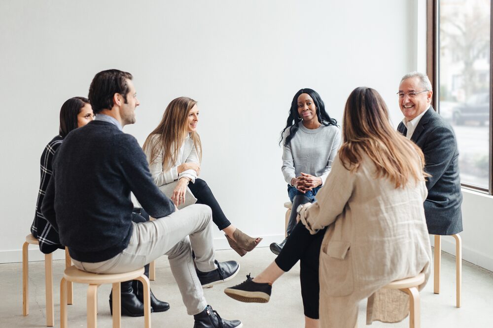 Team seated on stools in conversation beside a window
