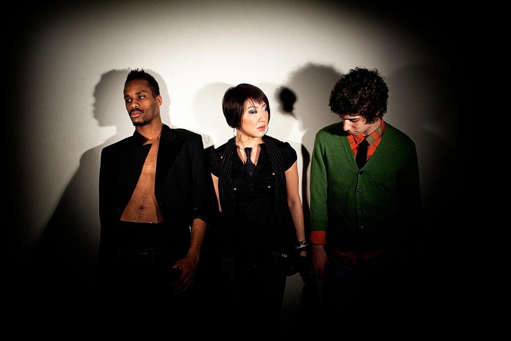 Three musicians in dark jackets under a spotlight
