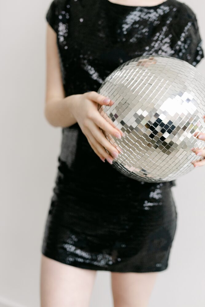 Woman in a black sequin dress holding a disco ball