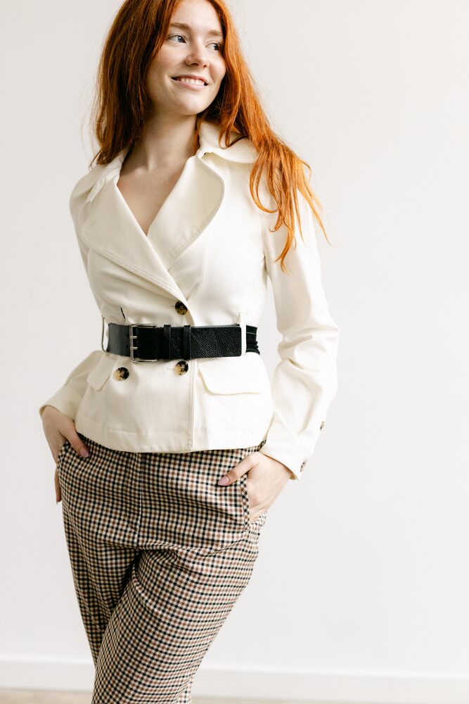 Woman with red hair in a white belted blazer and checked trousers