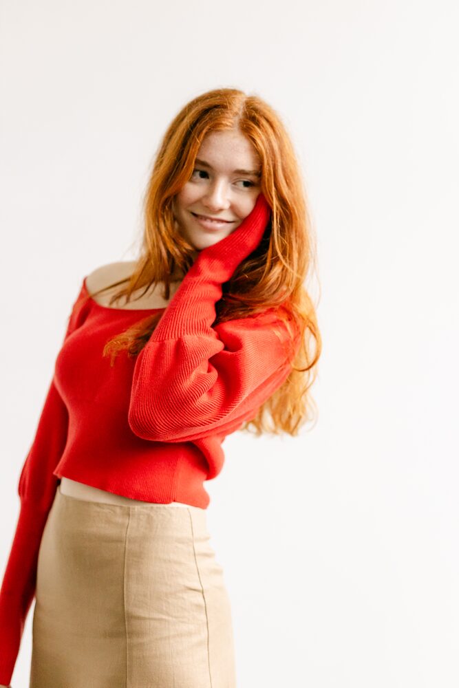 Woman with red hair in a red off-the-shoulder sweater, hand in her hair