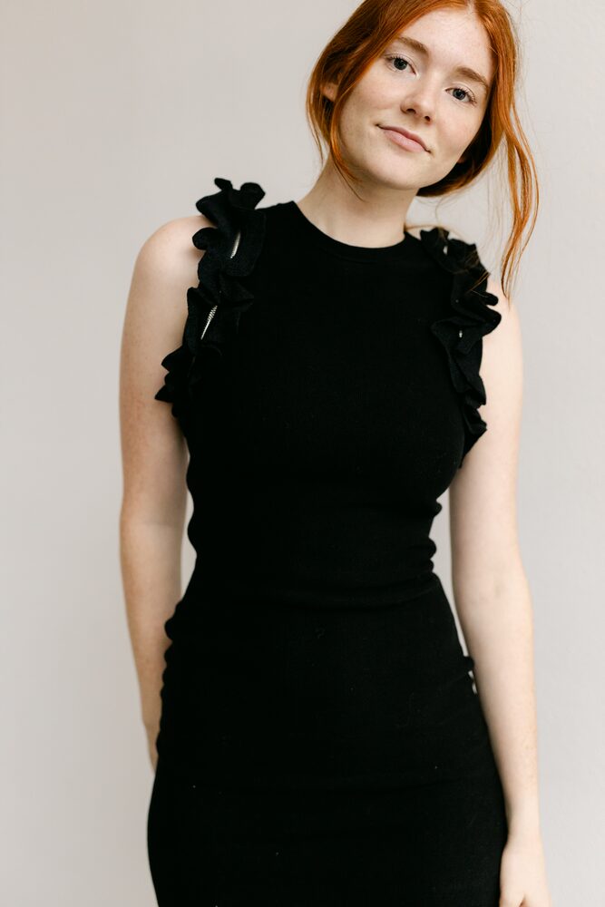 Woman with red hair in a black ruffled top against a white wall