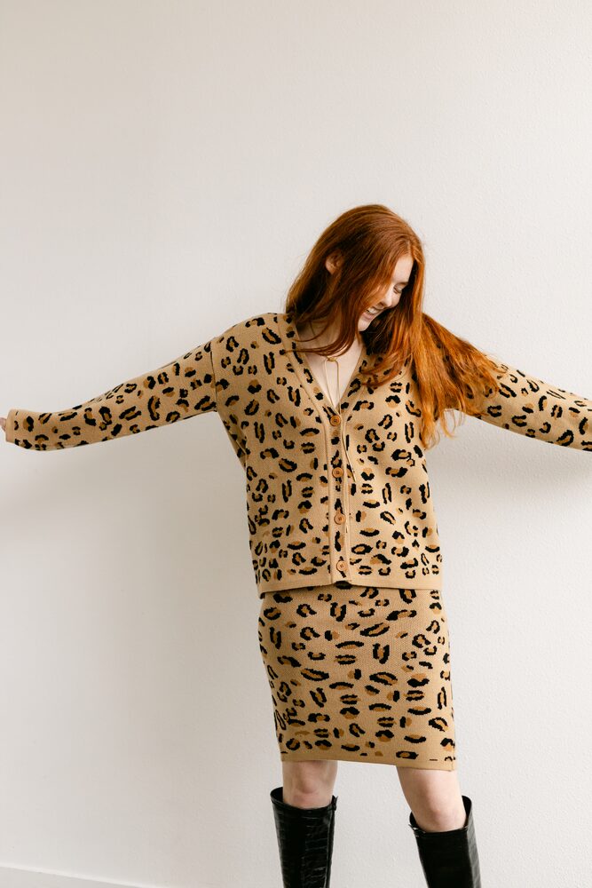 Woman with red hair in a leopard-print cardigan and skirt, arms outstretched