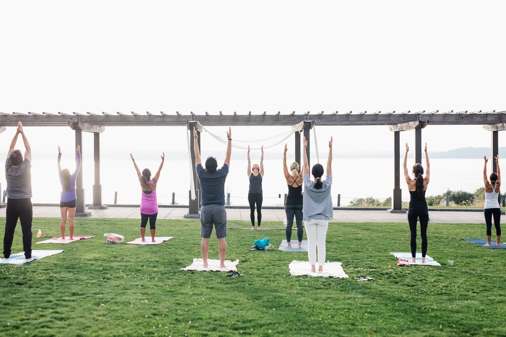 Yoga class stretching upward in front of a pergola by the water