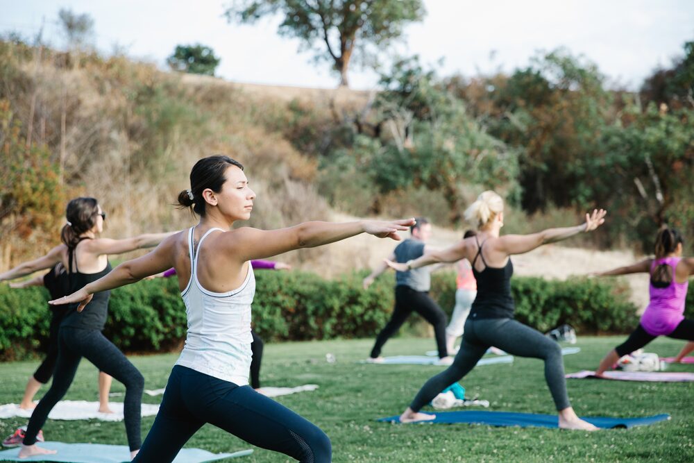 Yoga class holding warrior pose on a lawn