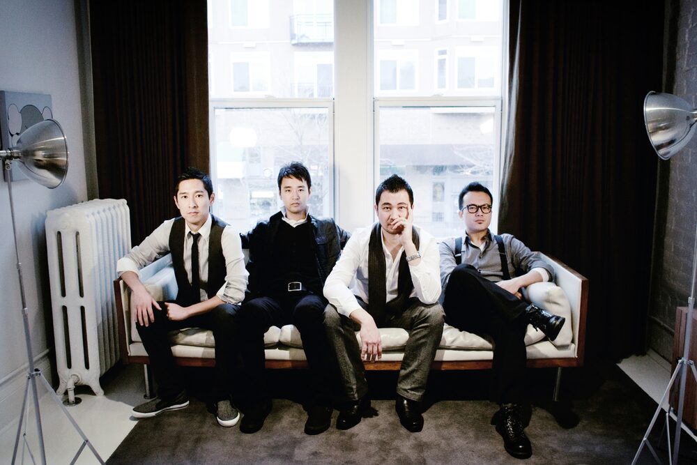 Four-piece band seated on a sofa in front of a window