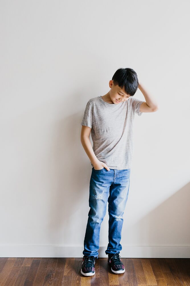 Boy in a grey t-shirt and jeans standing against a white wall
