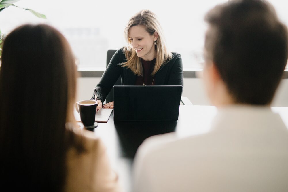 Woman leading a meeting across a table with a laptop and coffee
