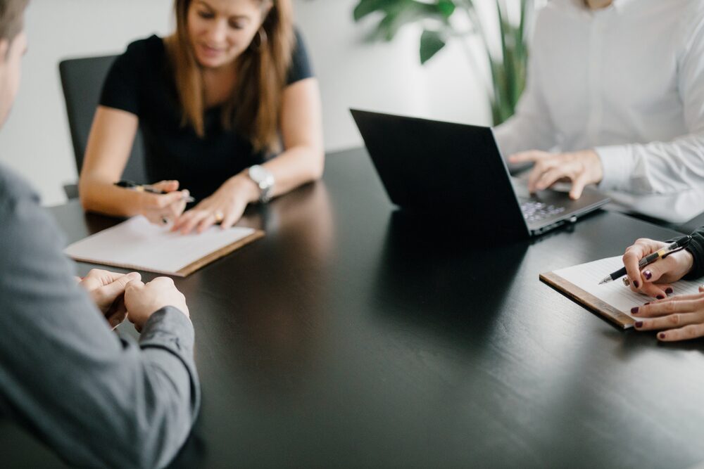 Hands taking notes and typing at a dark conference table