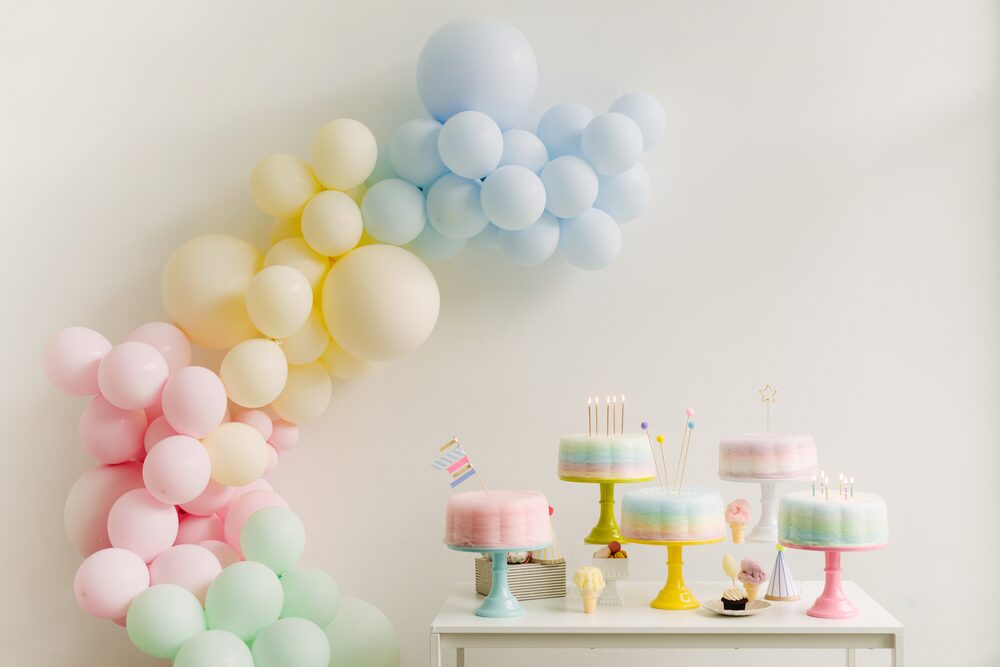 Pastel balloon arch above a table of birthday cakes