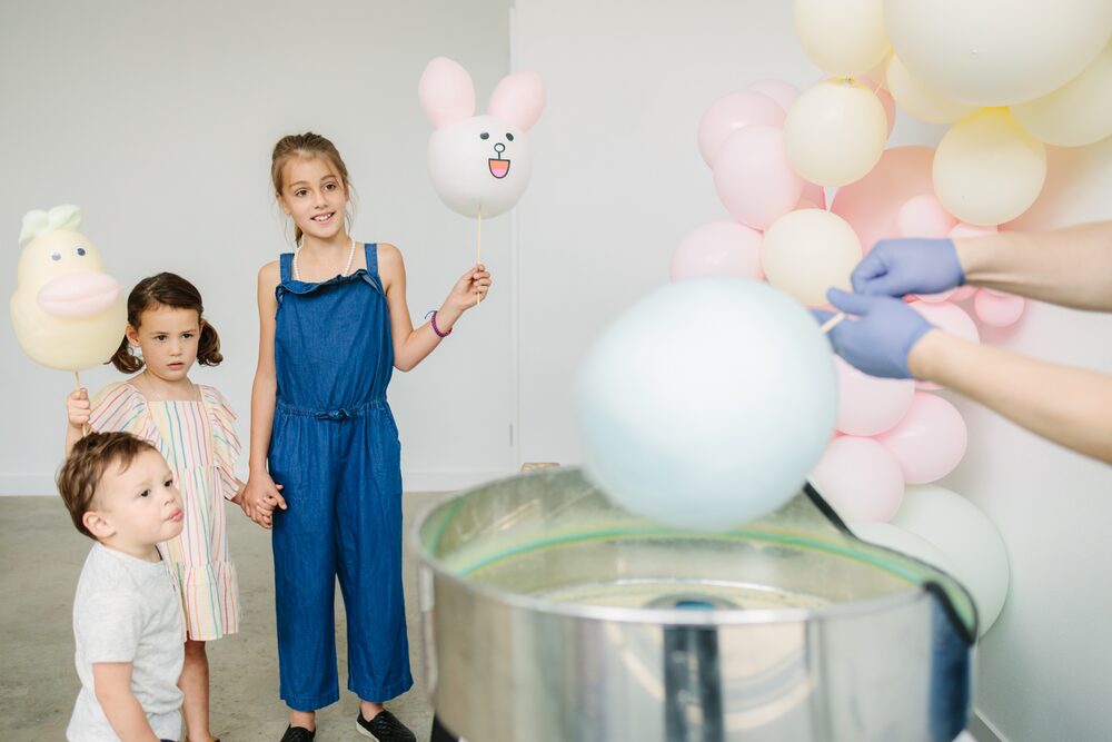 Children holding balloons beside a table of cakes
