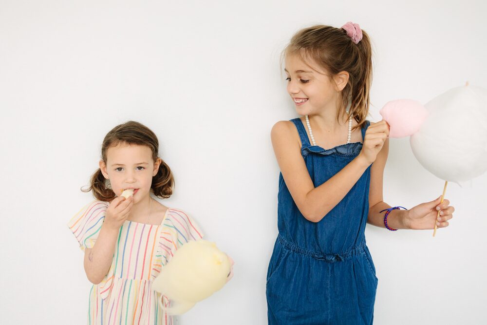 Two girls in a striped dress and blue overalls holding cotton candy