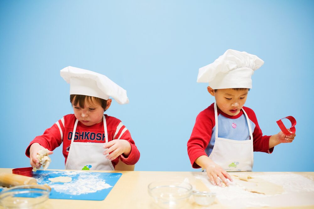 Two boys in chef hats cutting cookie dough with cutters