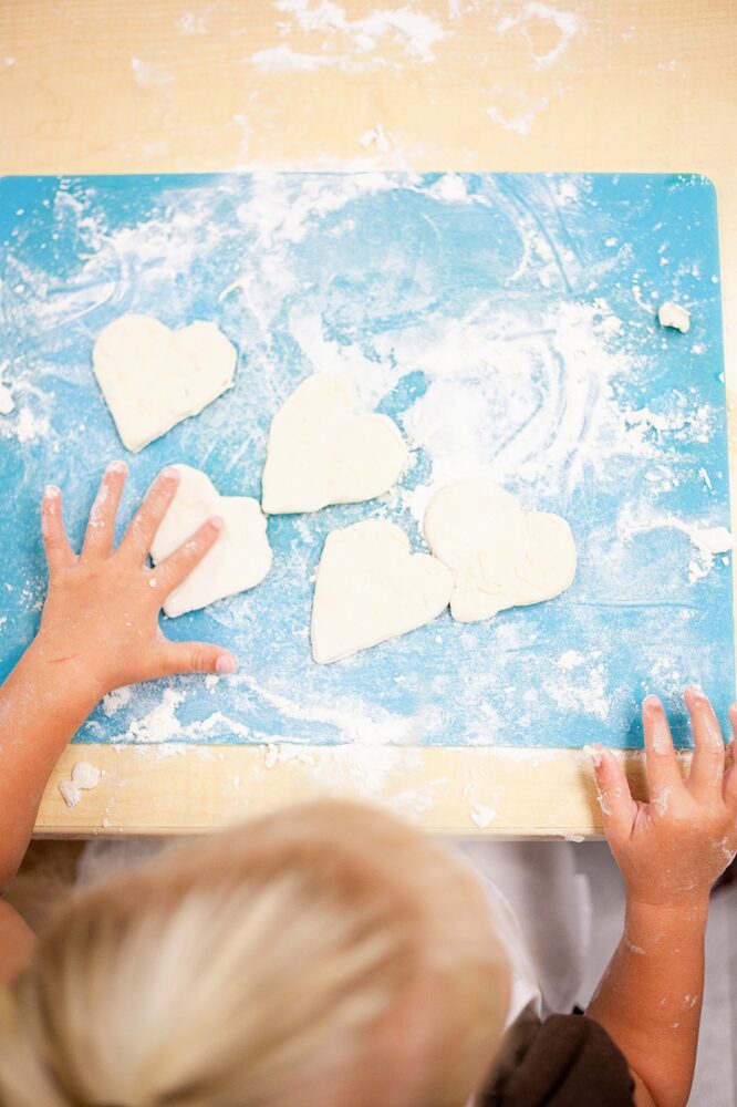 Overhead view of a child's hands cutting heart-shaped cookies in flour
