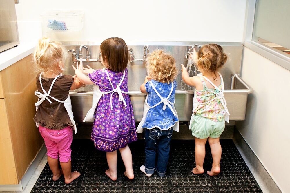Four children in aprons washing hands at a steel sink