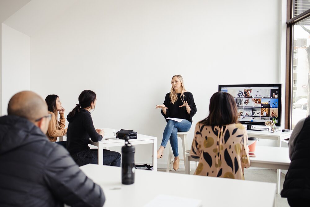 Presenter speaking to a small seated audience in a white studio