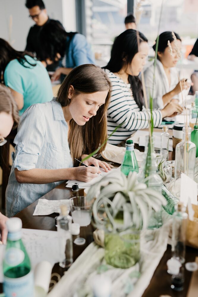 Guests seated at a workshop table with bottles and greenery