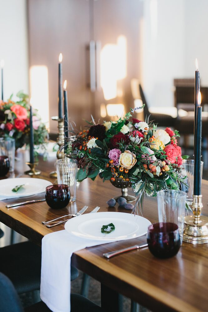 Dinner table set with dark candles and a colourful floral centrepiece