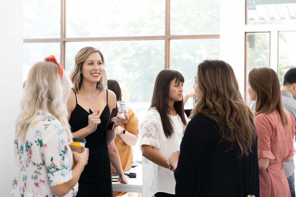 Women chatting beside tall windows at a daytime reception