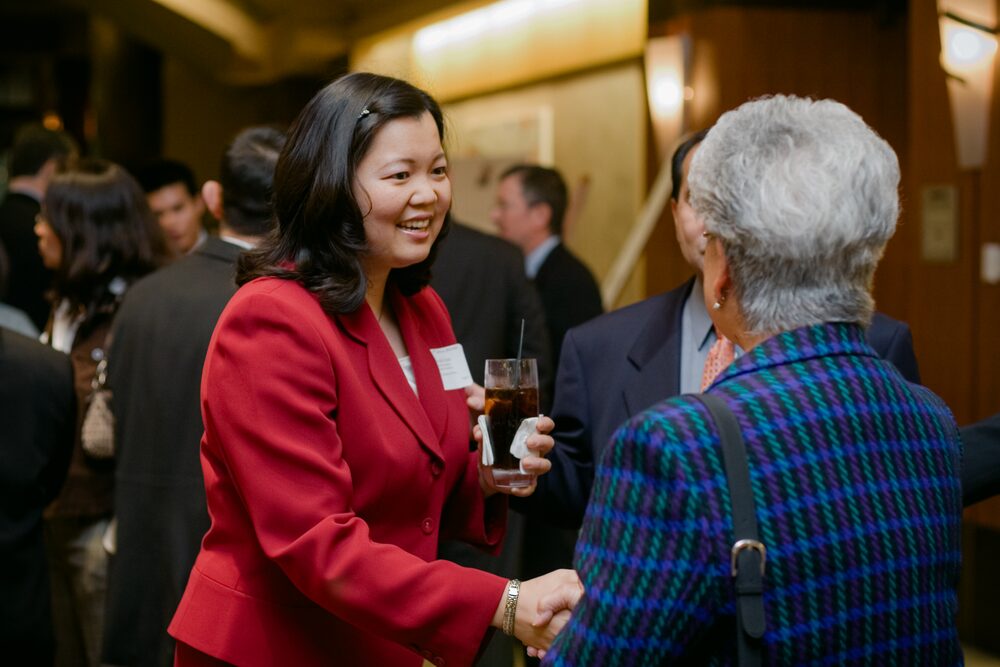 Two guests shaking hands at a reception, one in a red blazer