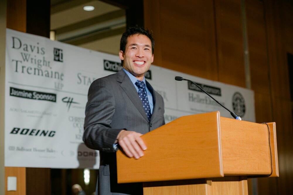 Speaker smiling at a podium in front of a sponsor banner