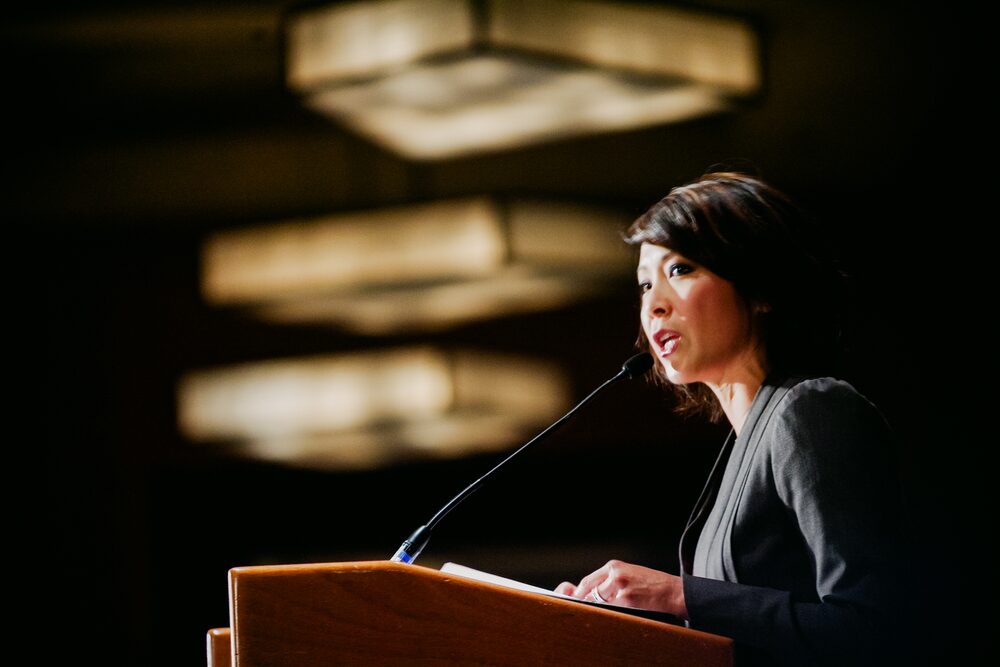Speaker at a podium under warm pendant lights