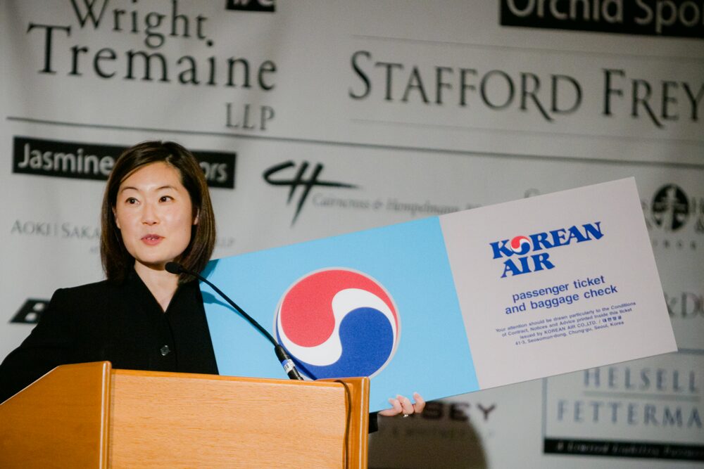 Speaker at a podium holding an oversized airline ticket