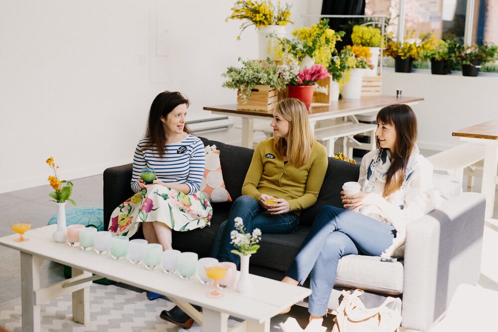 Three women seated on a sofa at a bright floral-themed gathering