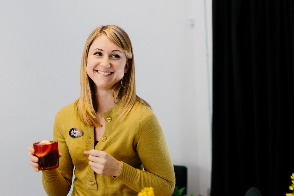 Woman in a mustard cardigan holding a drink and smiling