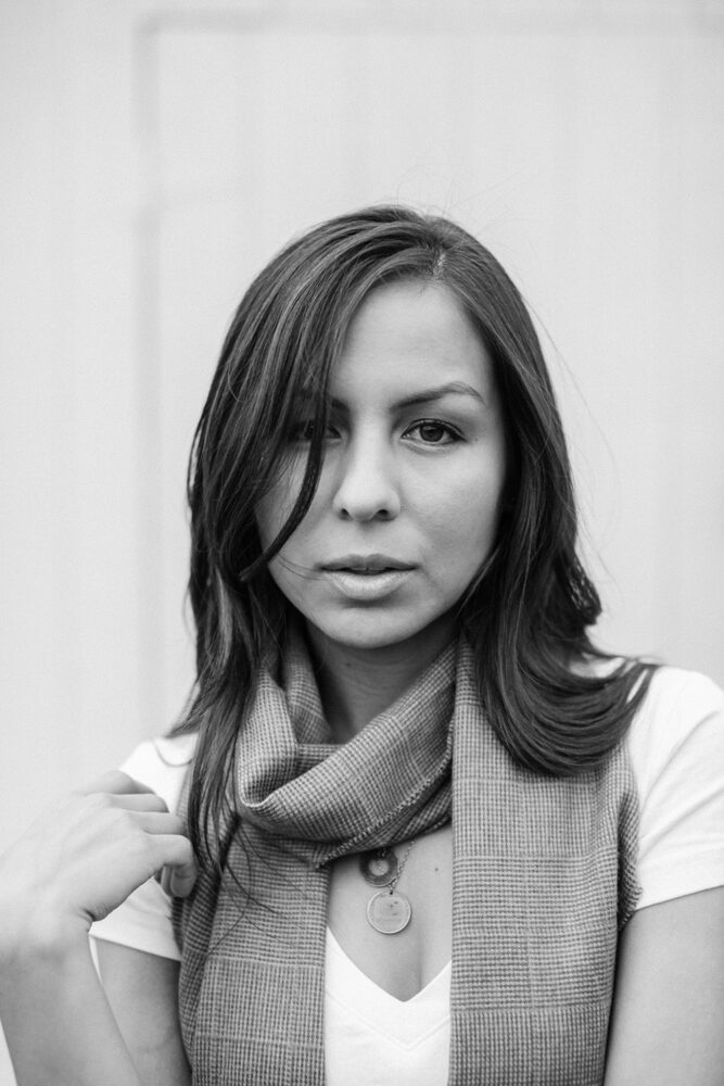 Black and white portrait of a woman with long dark hair and a scarf, looking at the camera