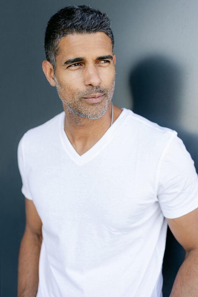 Man in a white v-neck t-shirt looking off to the side against a dark background