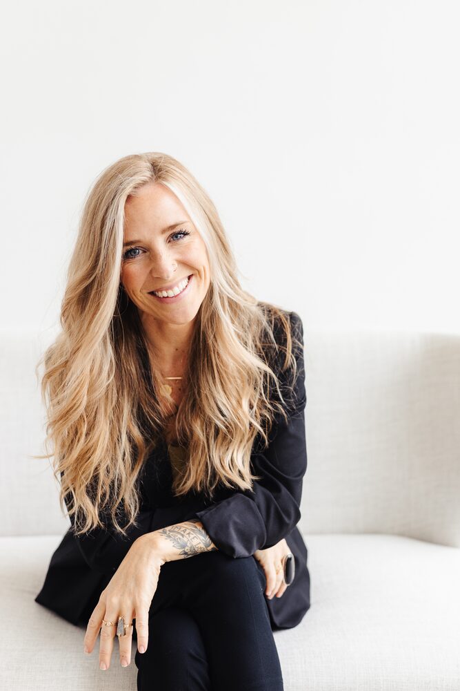 Woman with long blonde hair in a black blazer, seated and smiling