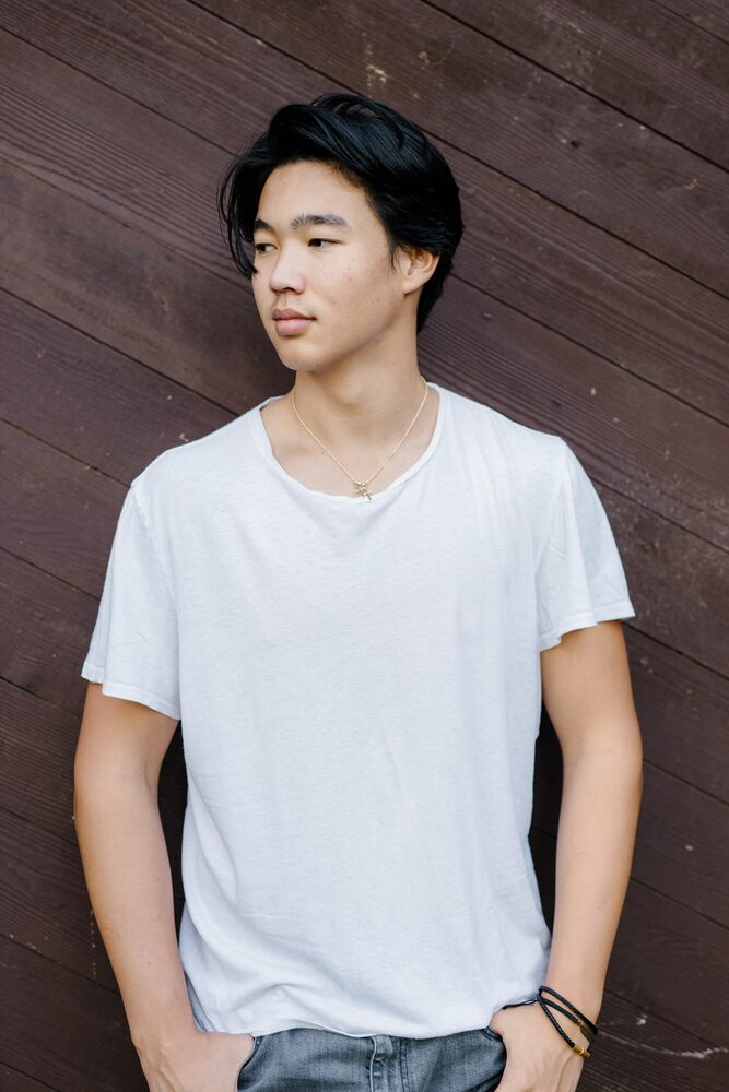 Young man in a white t-shirt leaning against a dark wood wall