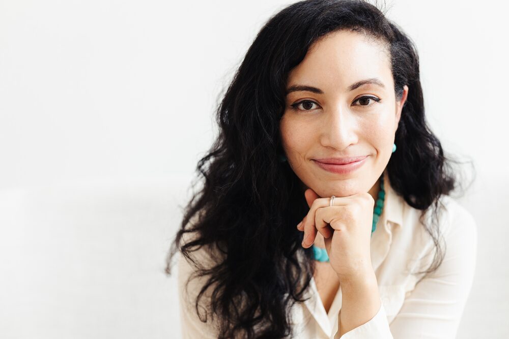 Woman with long dark hair resting her chin on her hand, smiling softly