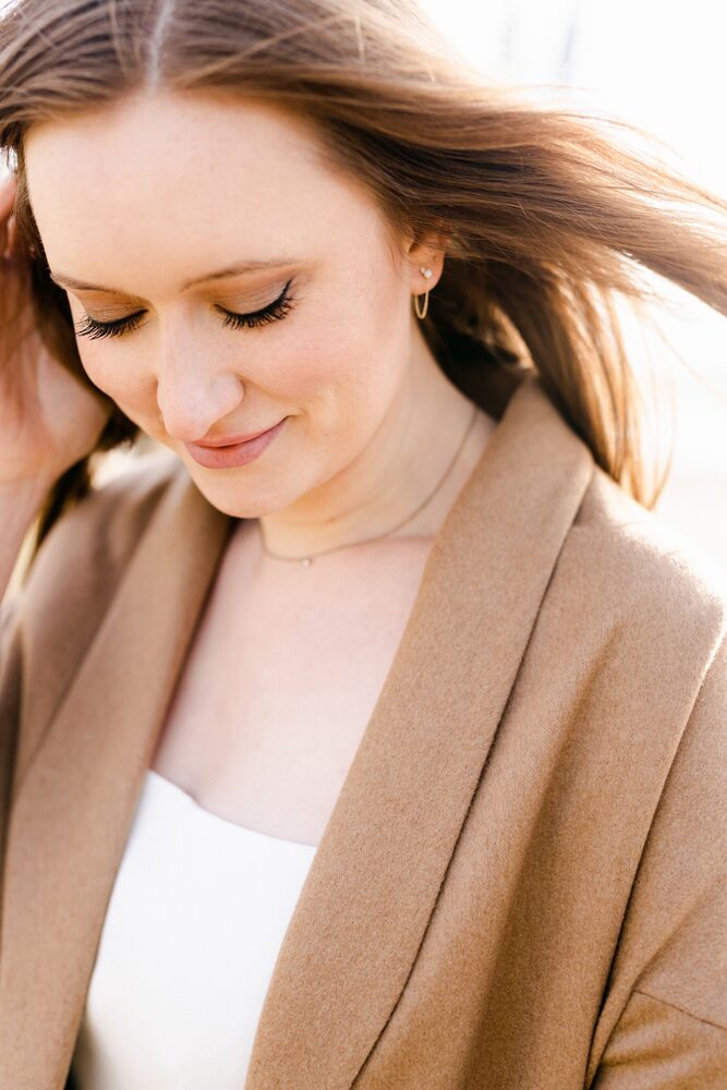 Woman with strawberry-blonde hair in a camel coat, looking down and smiling