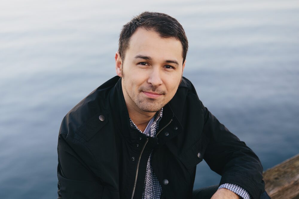 Man in a dark jacket seated at the water's edge
