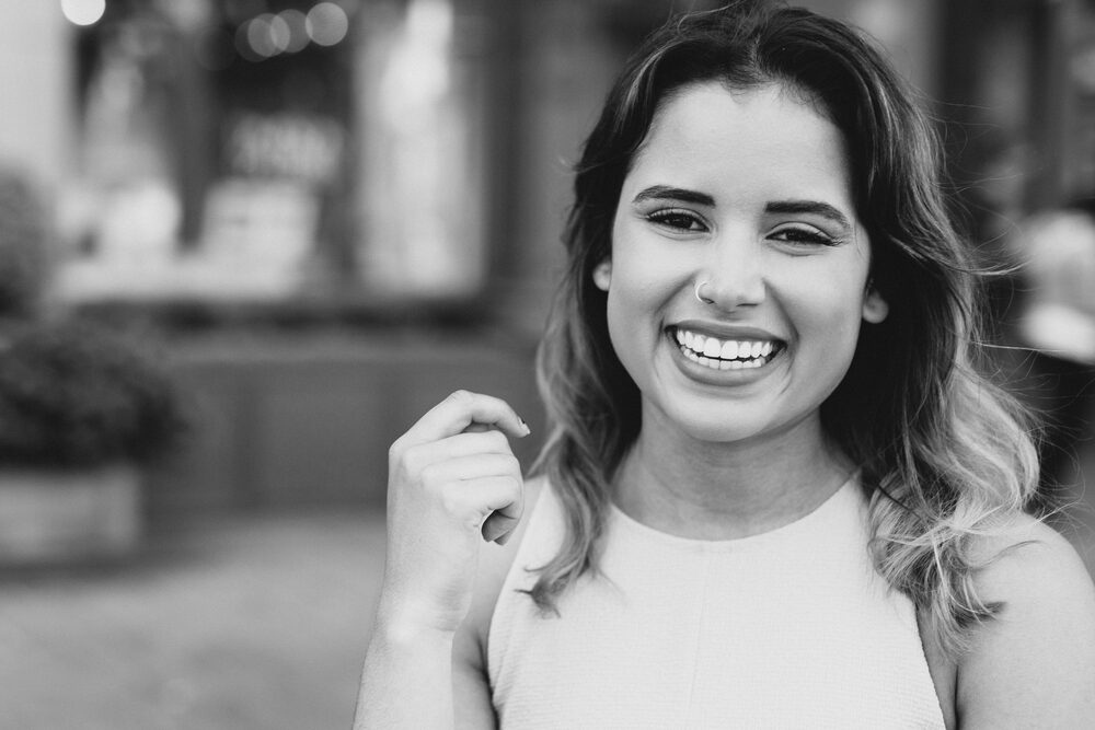 Black and white portrait of a laughing woman in a white top on a city street