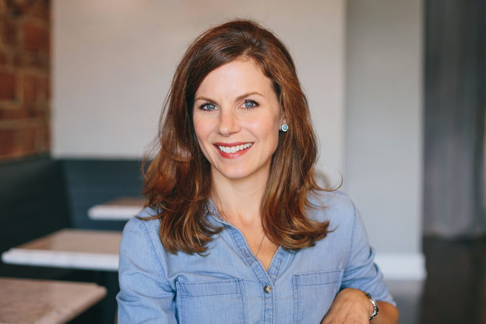 Woman with auburn hair in a chambray shirt, smiling in a café