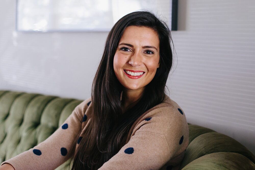 Woman with long dark hair in a polka-dot sweater on a green velvet sofa