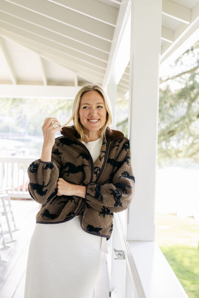 Woman in a patterned jacket and white skirt on a covered porch by the water