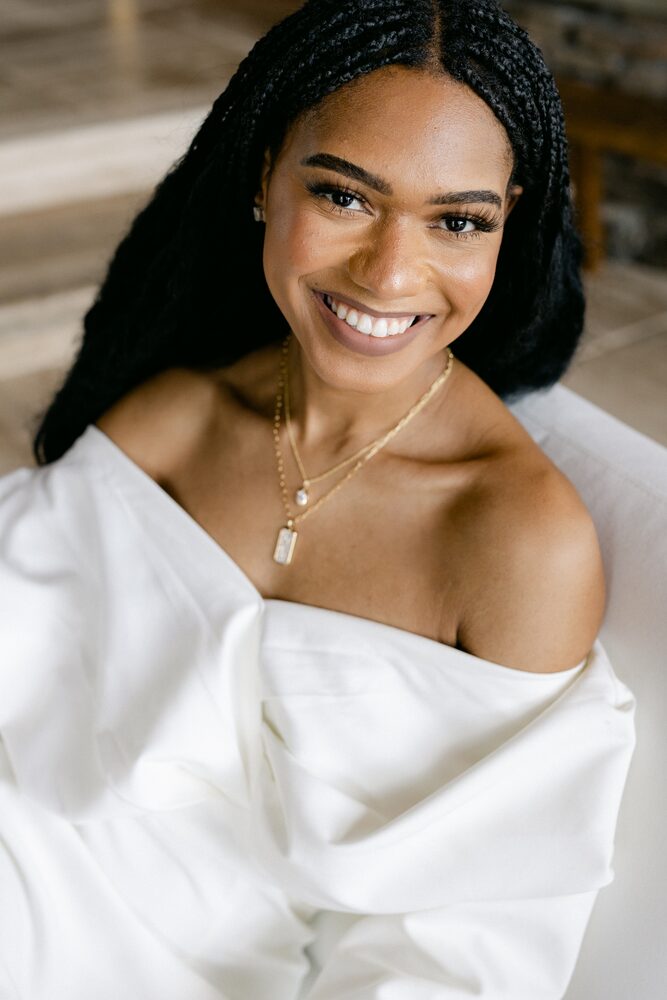 Woman with braids in an off-the-shoulder white top, smiling warmly