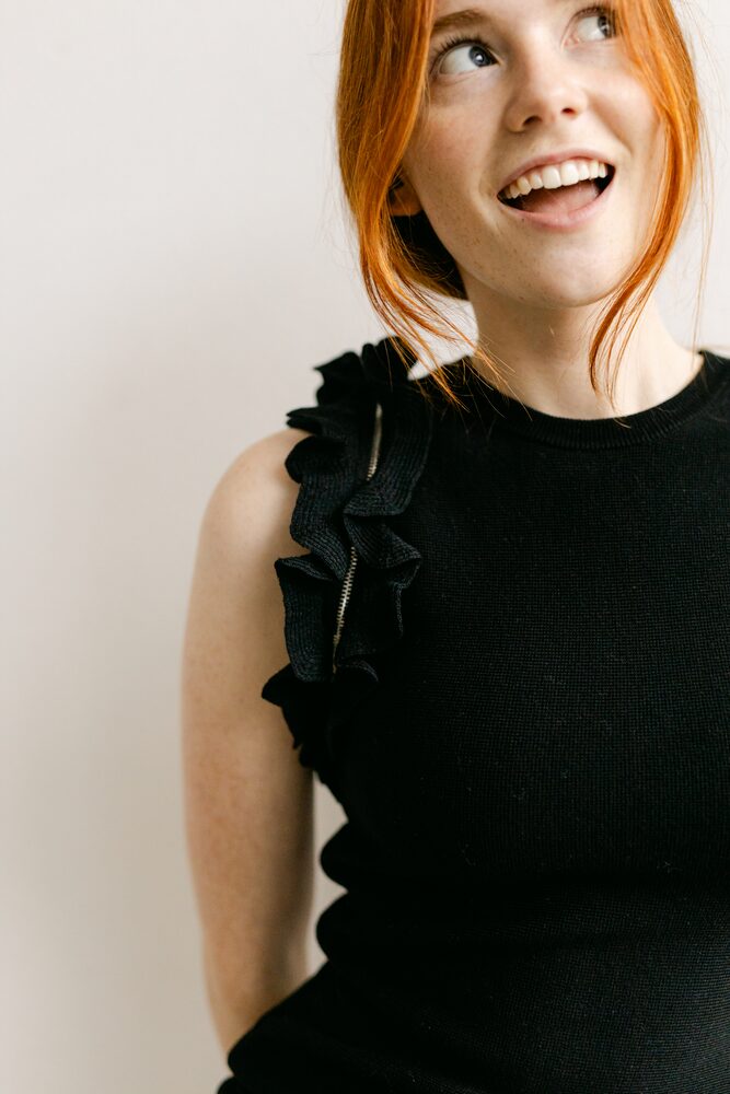 Woman with red hair in a black ruffled top, laughing and looking up