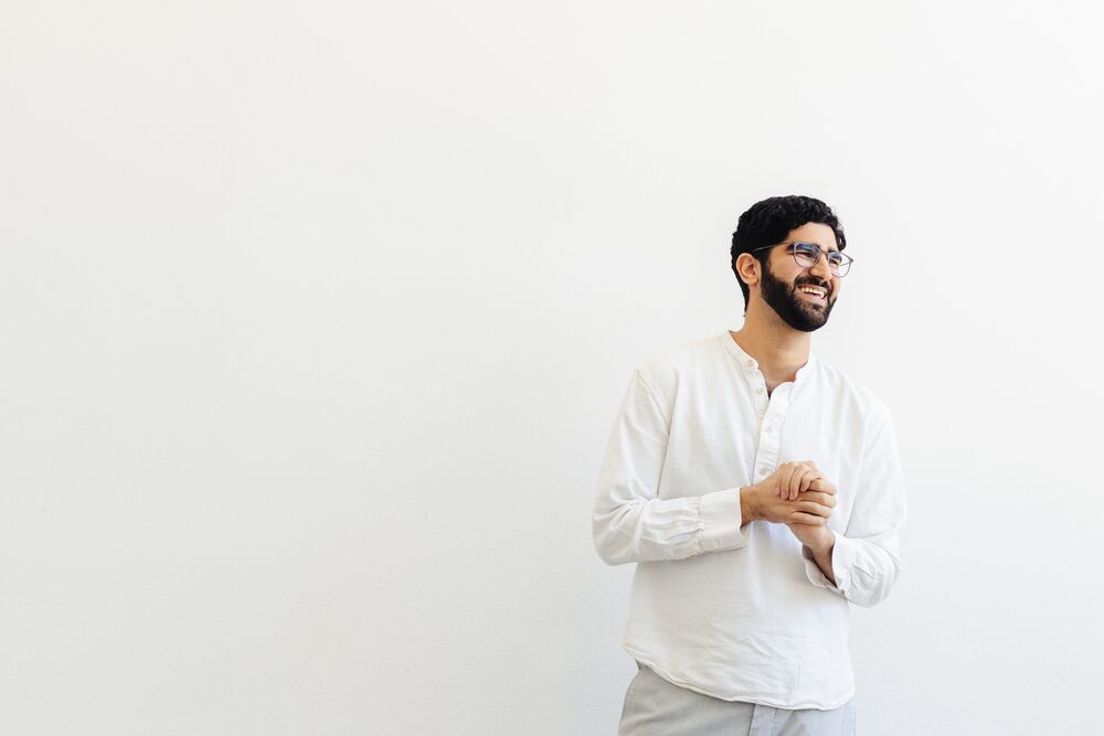 Man in a white shirt and glasses laughing against a white background