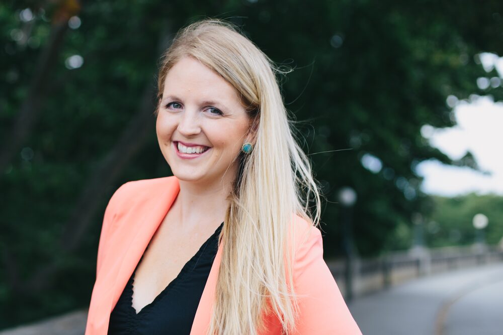 Woman with long blonde hair in a coral blazer smiling outdoors