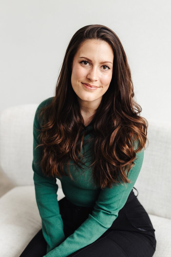 Woman with long dark hair in a green sweater seated on a white sofa