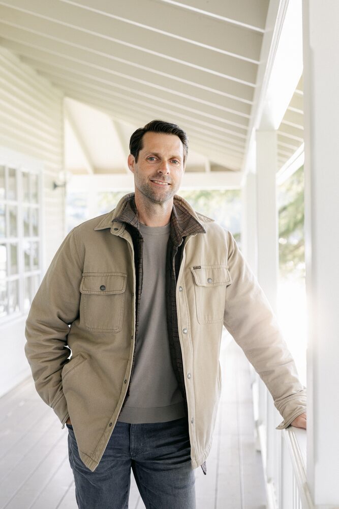 Man in a tan jacket standing on a white porch