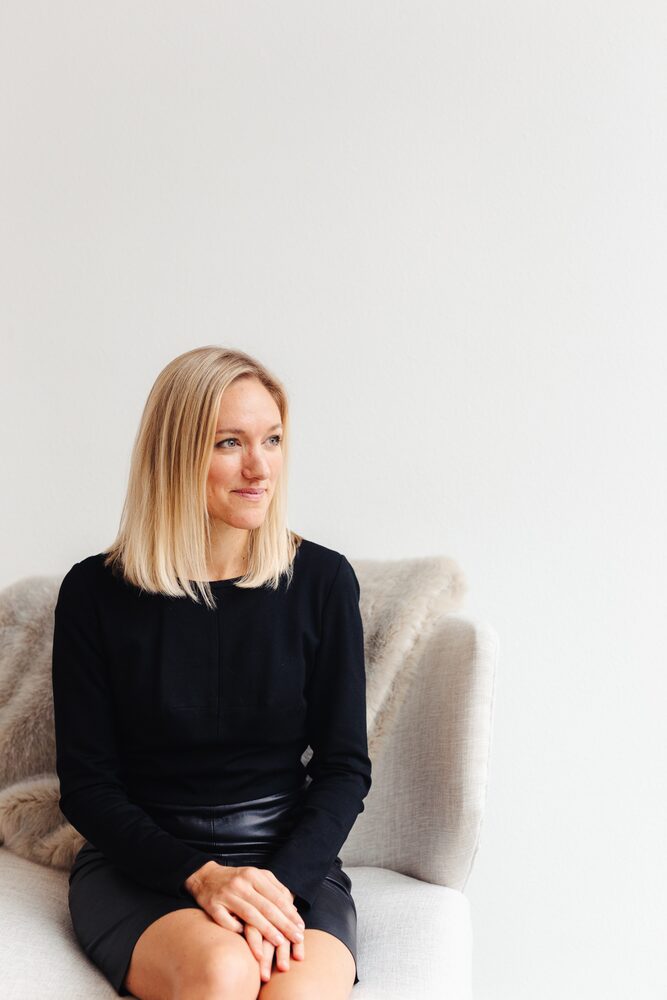 Woman with blonde hair in a black dress seated on a light armchair