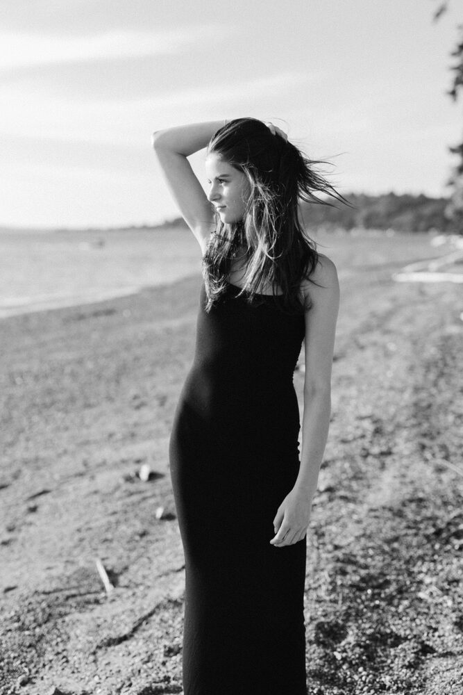 Black and white photo of a woman in a long black dress on a beach, hand in her hair