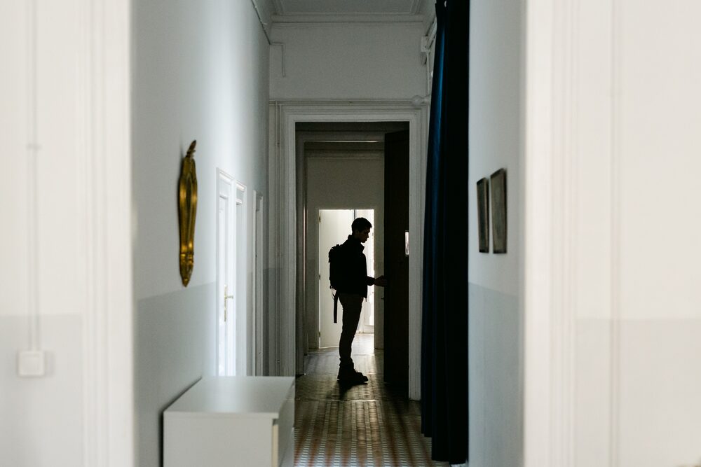 Silhouetted figure in a doorway at the end of a bright hallway